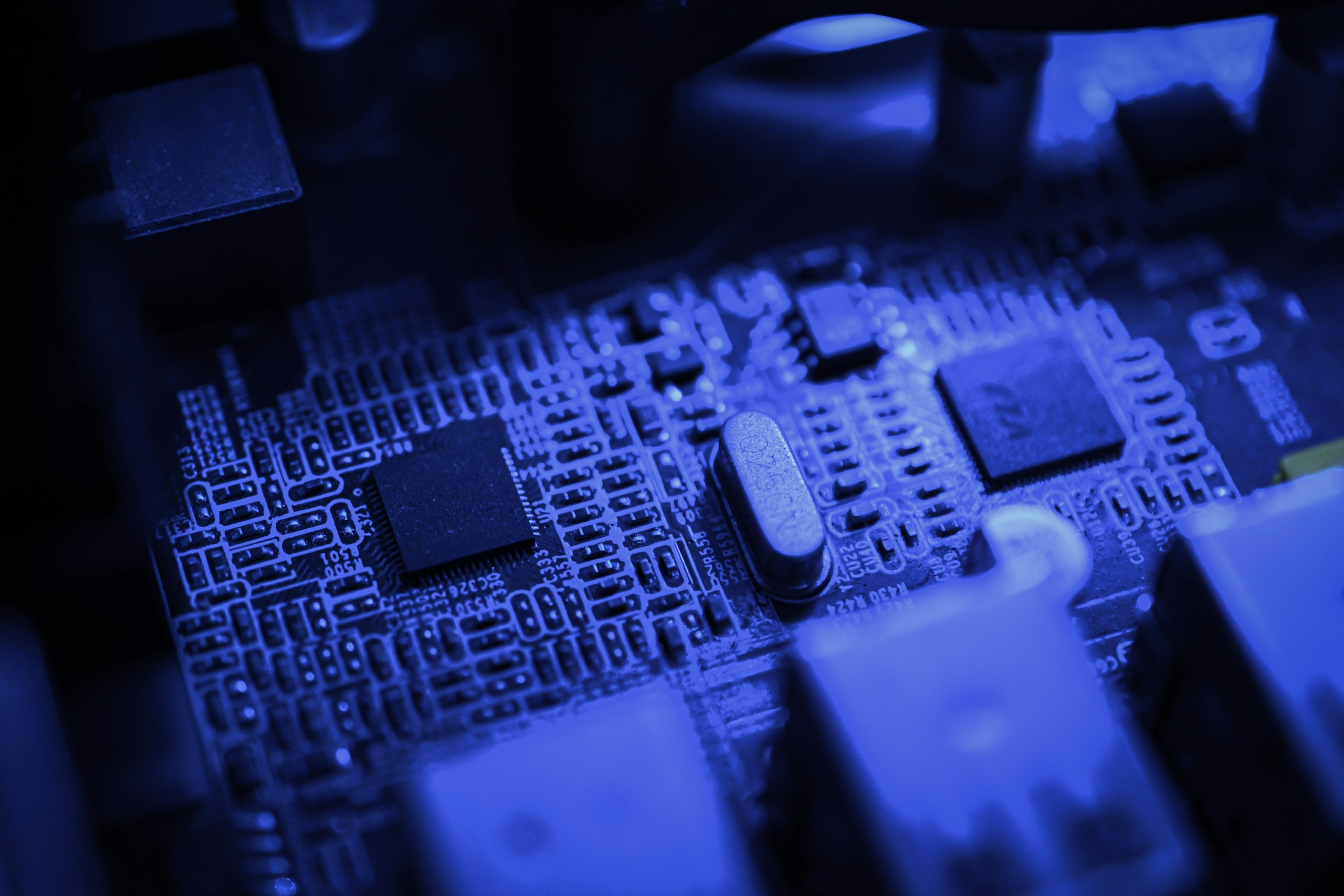 A closeup of the inside of a computer, with a focus on the circuit board, in blue light.